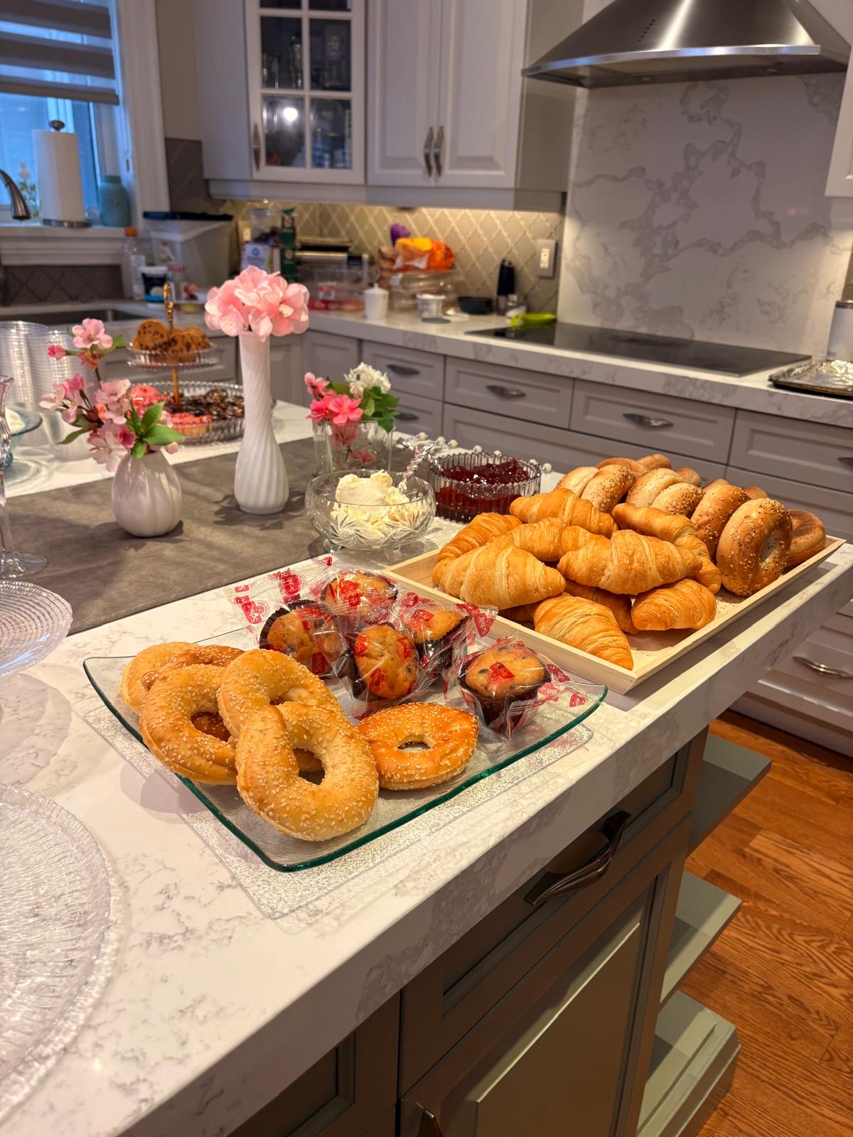 Breakfast buffet of bagels, muffins, and croissants with pink floral centerpieces