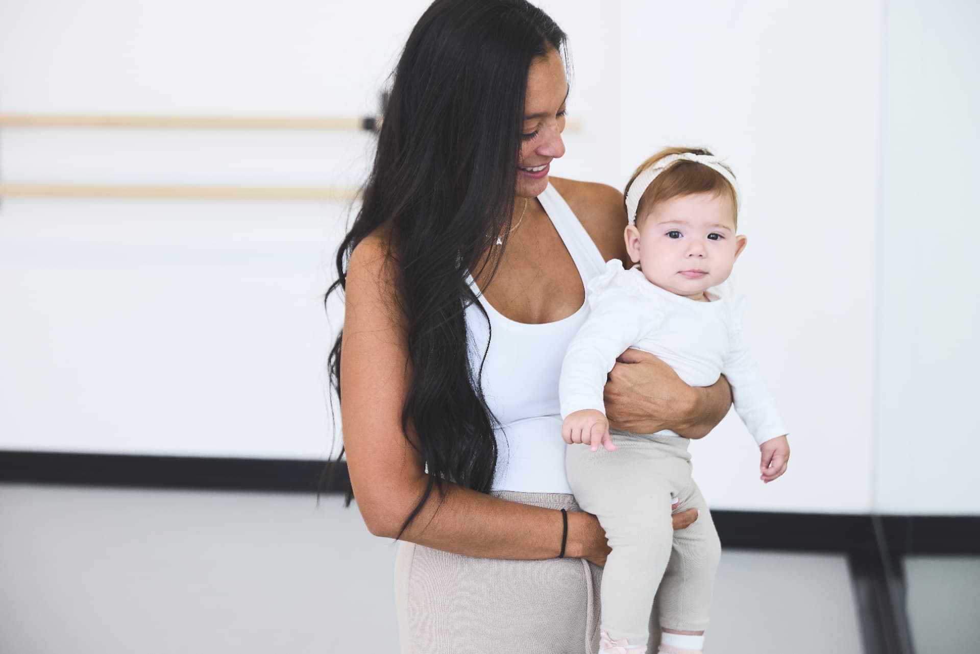 Mom smiling at her baby beside the studio barre