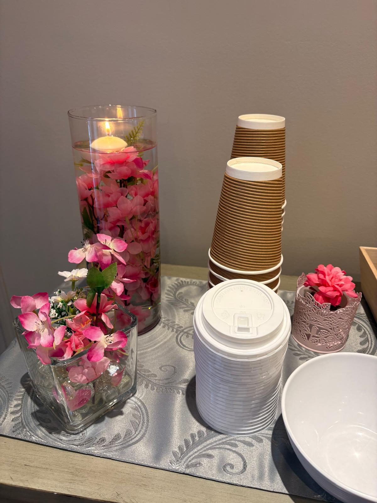 Drink station with stacked cups, lids, and a vase of pink blossoms