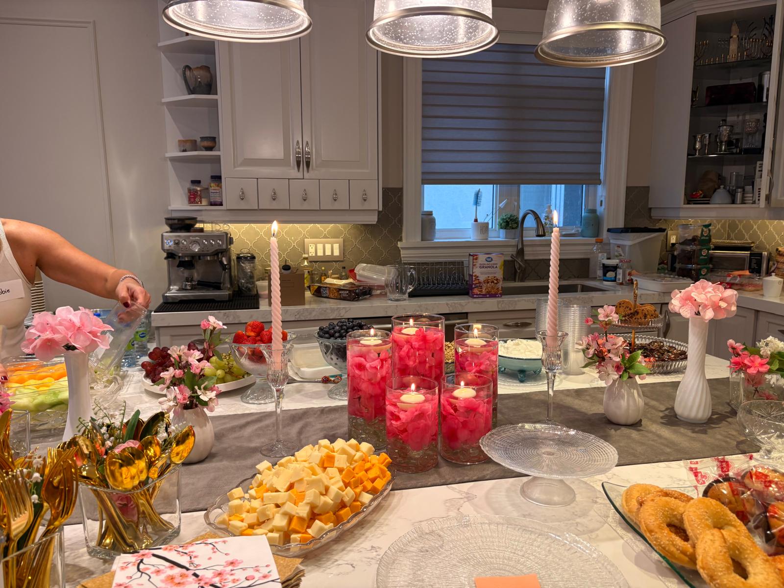 Brunch counter being set up with pastries, pink flowers, and lit candles