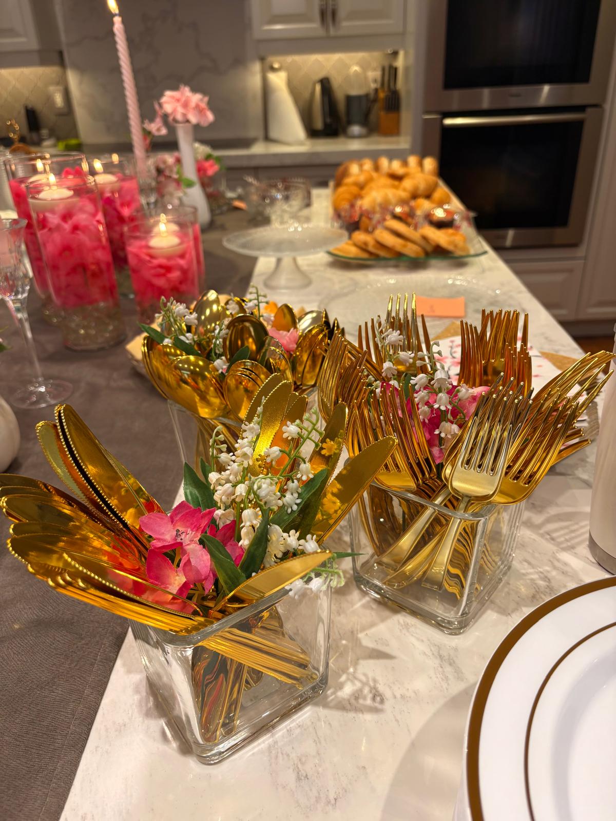 Glass vases of gold cutlery decorated with pink and white flowers beside the buffet