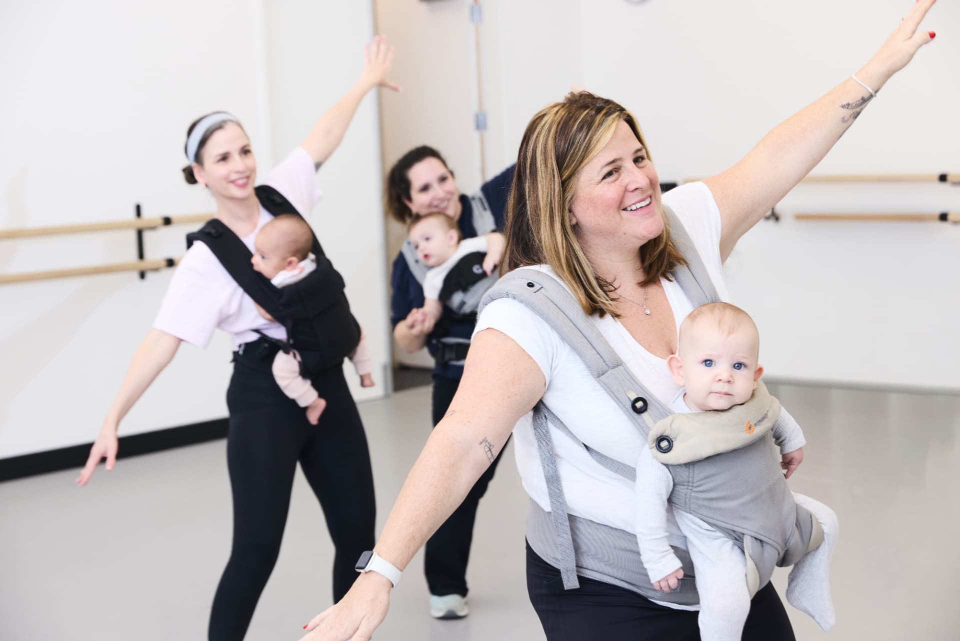 Moms extending their arms while dancing with babies in carriers